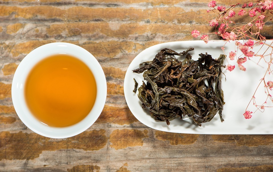 Image showing a cup of black tea with black tea leaves around it.
