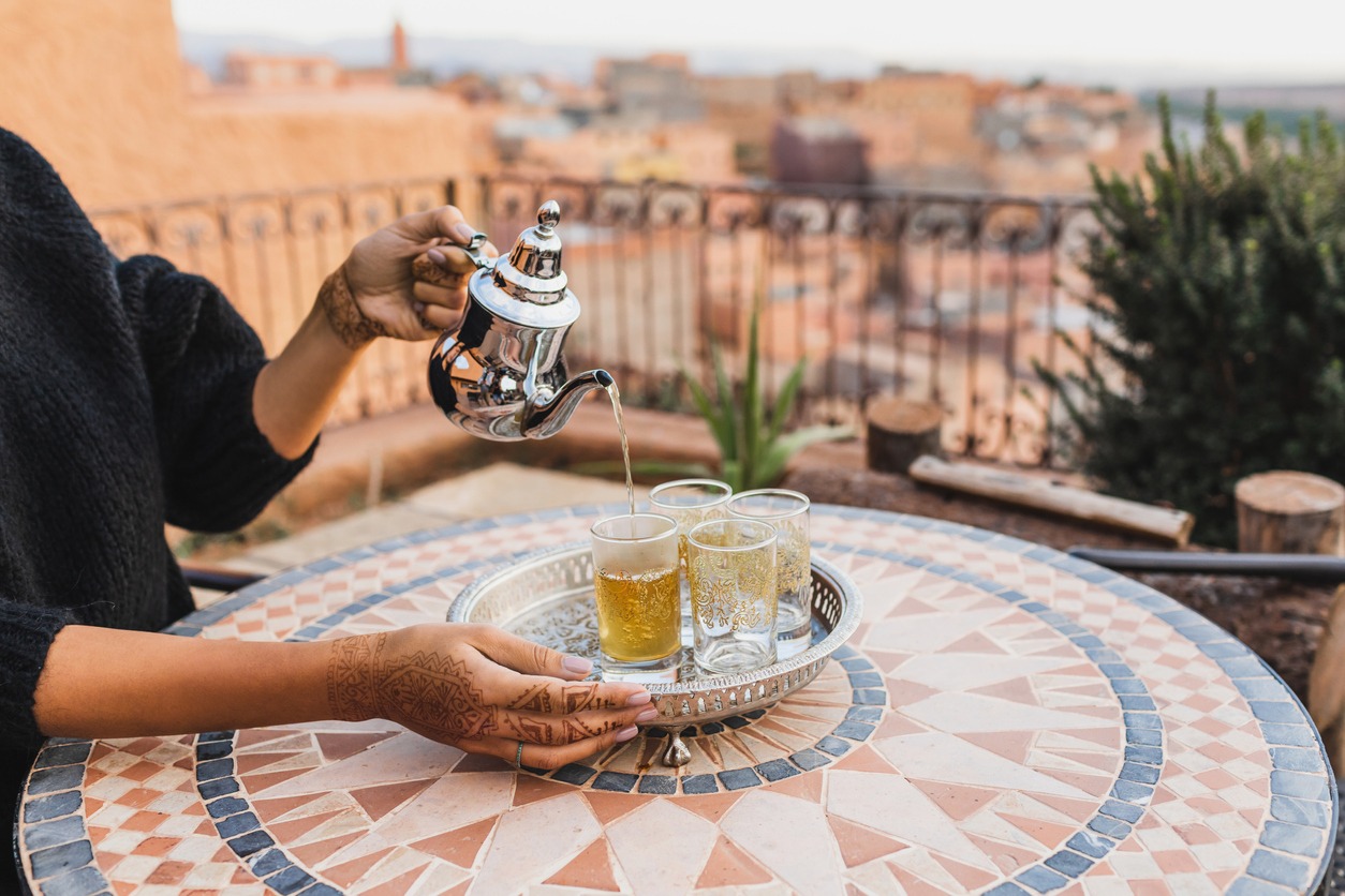 Woman hand pouring traditional moroccan mint tea in glasses. Vintage silver tray and teapot. Round mosaic table. Morocco hospitality.