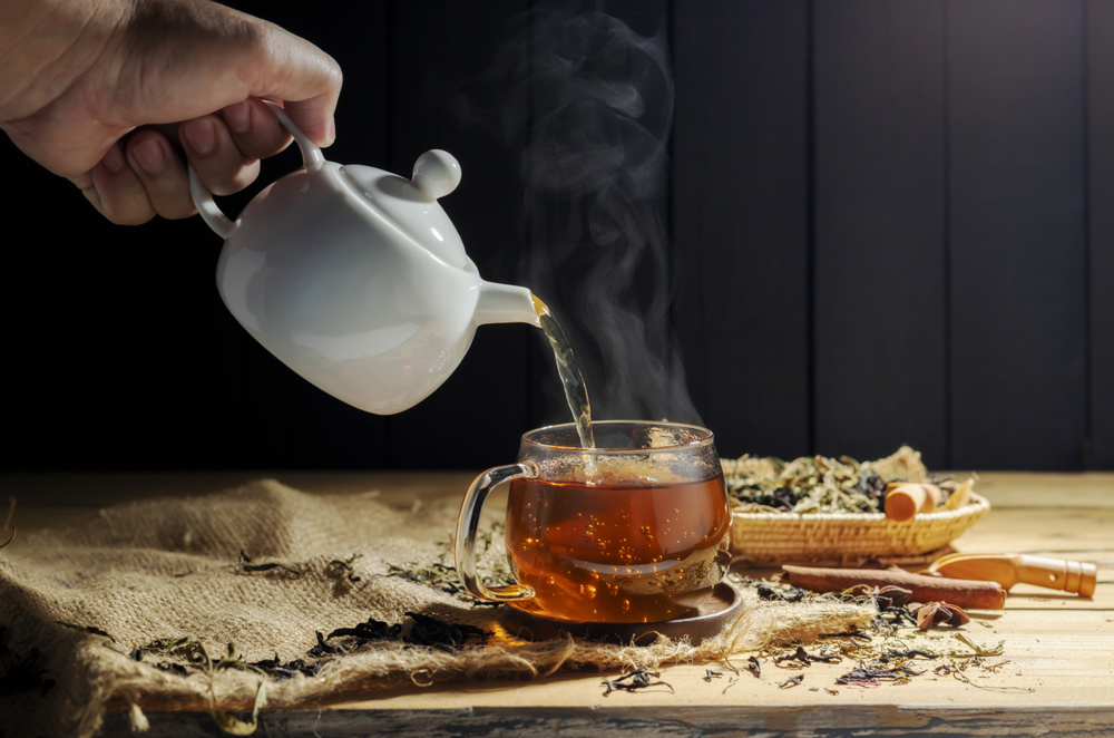 Pour hot tea into cups, herbal tea glasses are arranged on a rustic wooden table