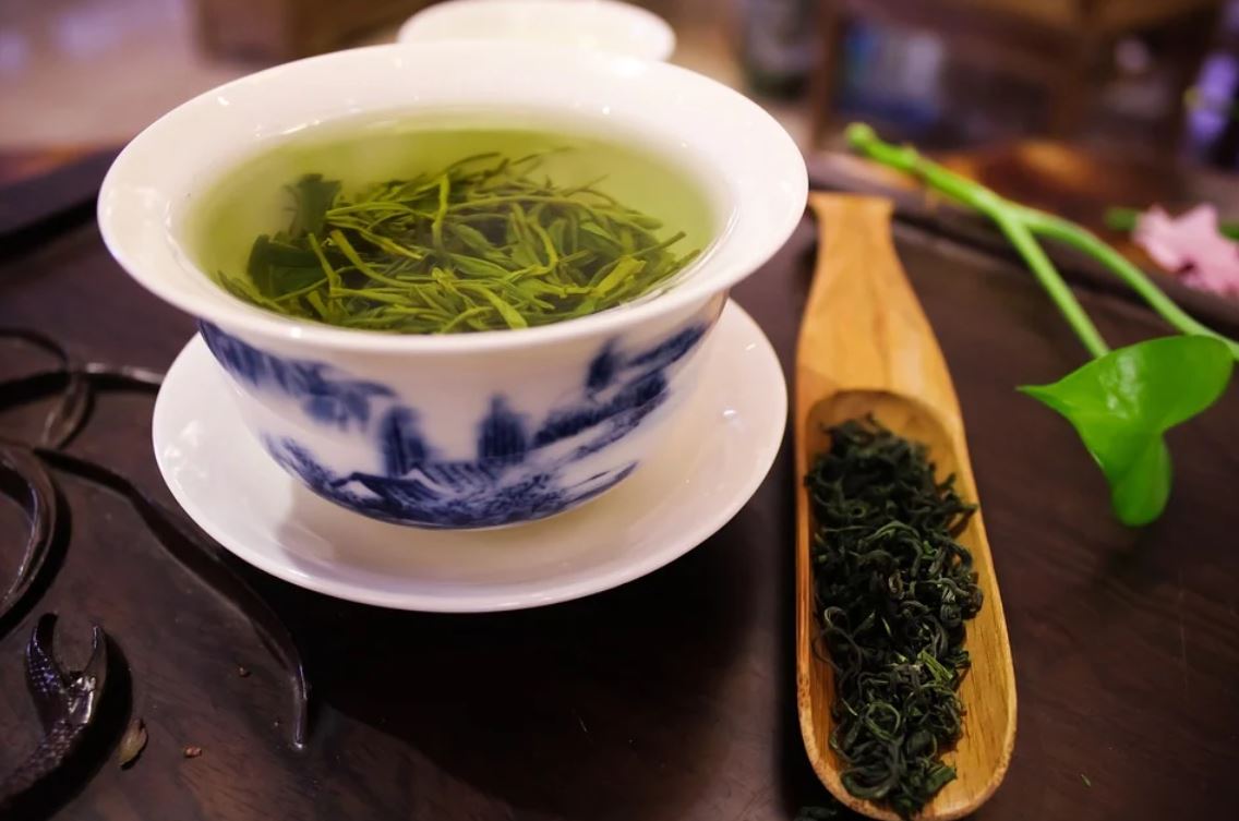 Image showing a cup of green tea with green tea leaves around it.
