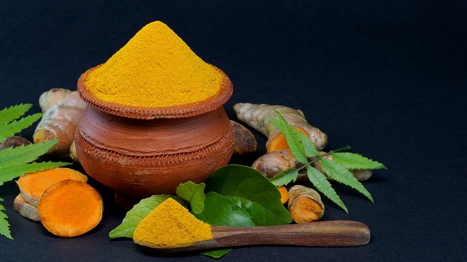 Image showing a pot full of turmeric powder surrounded by turmeric roots