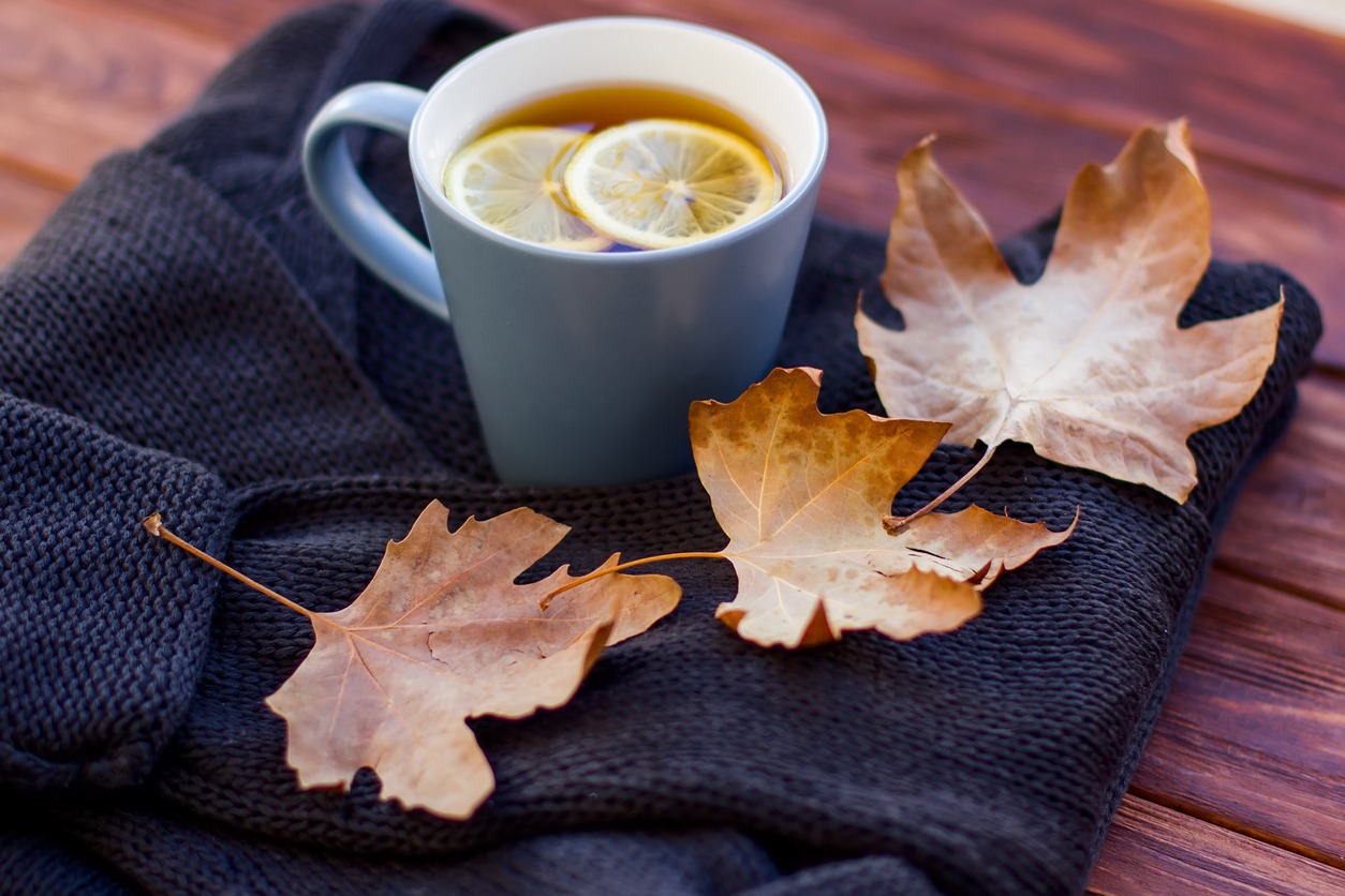 Autumn layout with hot tea with a lemon on a sweater and dry leaves.